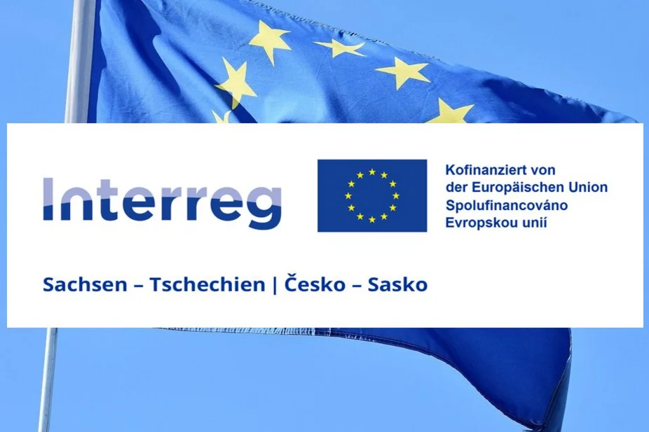EU-Flagge im Wind, darüber das INTERREG Sachsen-Tschechien-Logo