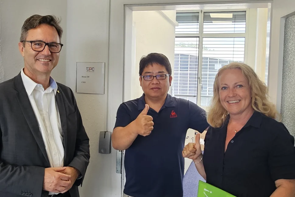 WFS-Geschäftsführer Thomas Horn und Cornelia Probst, Mitarbeiterin im Bereich Investorenservice bei der WFS, gratulieren dem Geschäftsführer von TPC Germany GmbH, West Tu, zum ersten Geburtstag der Firma am Standort Dresden.